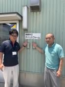 建物外壁の看板を指さす金屋本江アイリスファーム 副代表理事 中島龍二さん